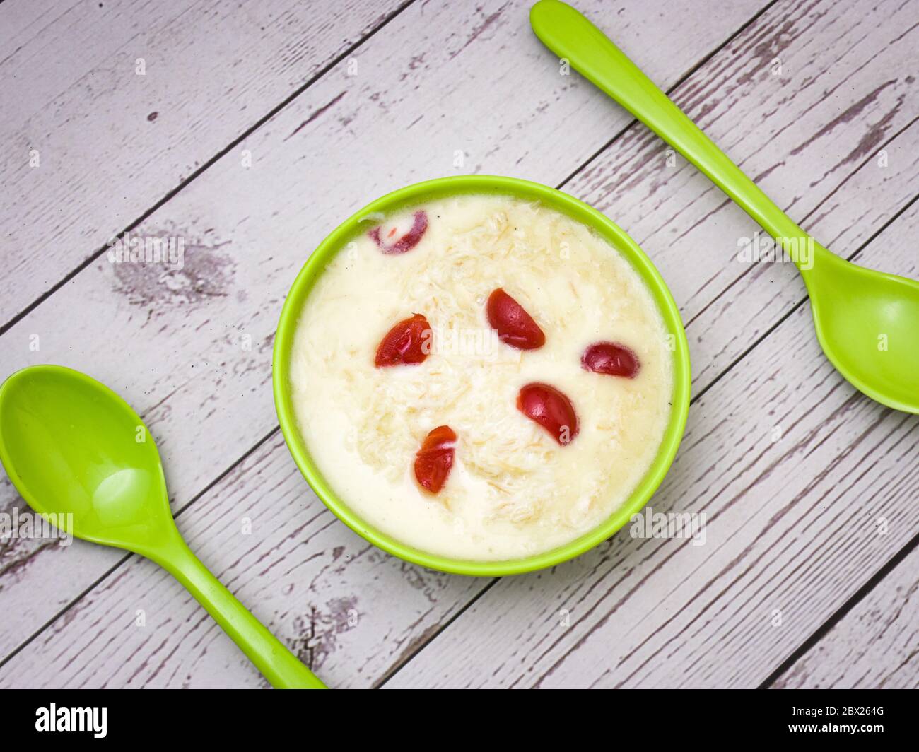Sewai o kheer consumati in occasione di festival eid o indiani. Servito con condimenti di ciliegia rossa in una ciotola verde. Foto Stock