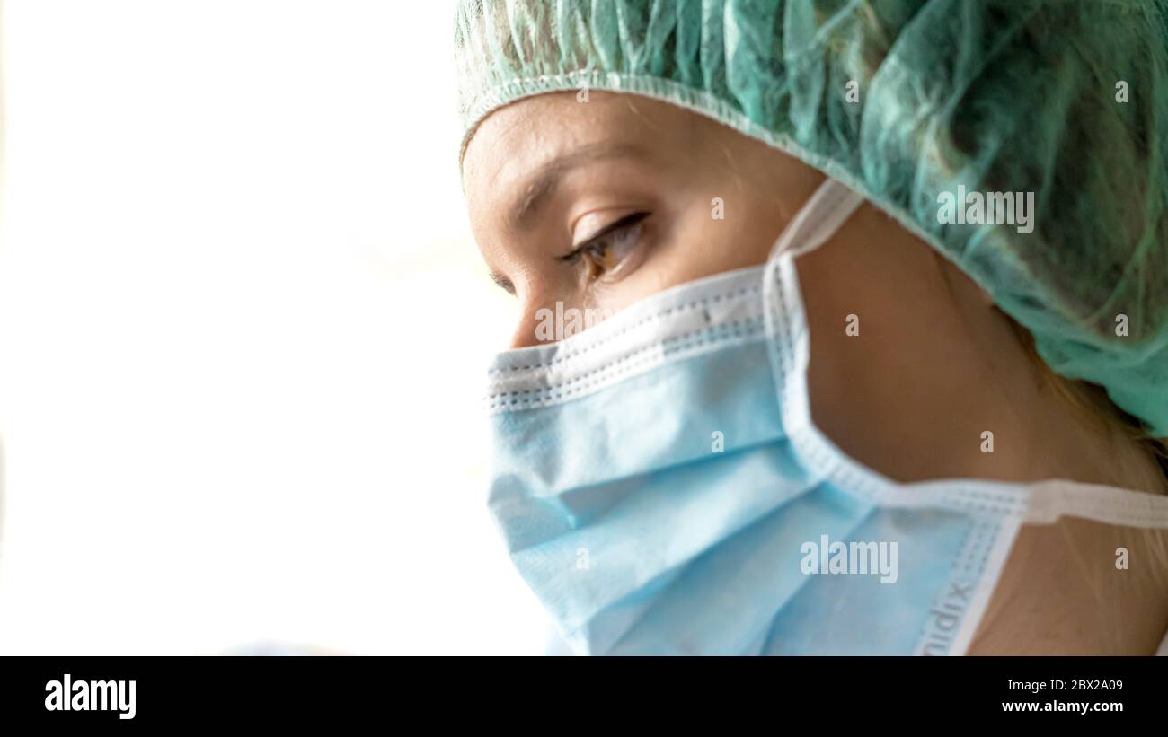 Una donna, preoccupata dottoressa in tuta protettiva, guardando attraverso la finestra dell'ospedale Foto Stock