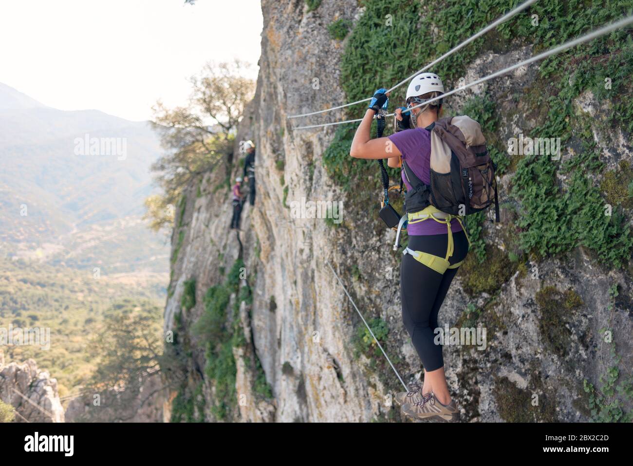 Concetto: Avventura. Donna con casco, imbracatura e zaino. Camminando su un ponte tibetano, facendo via ferrata in montagna. Foto Stock