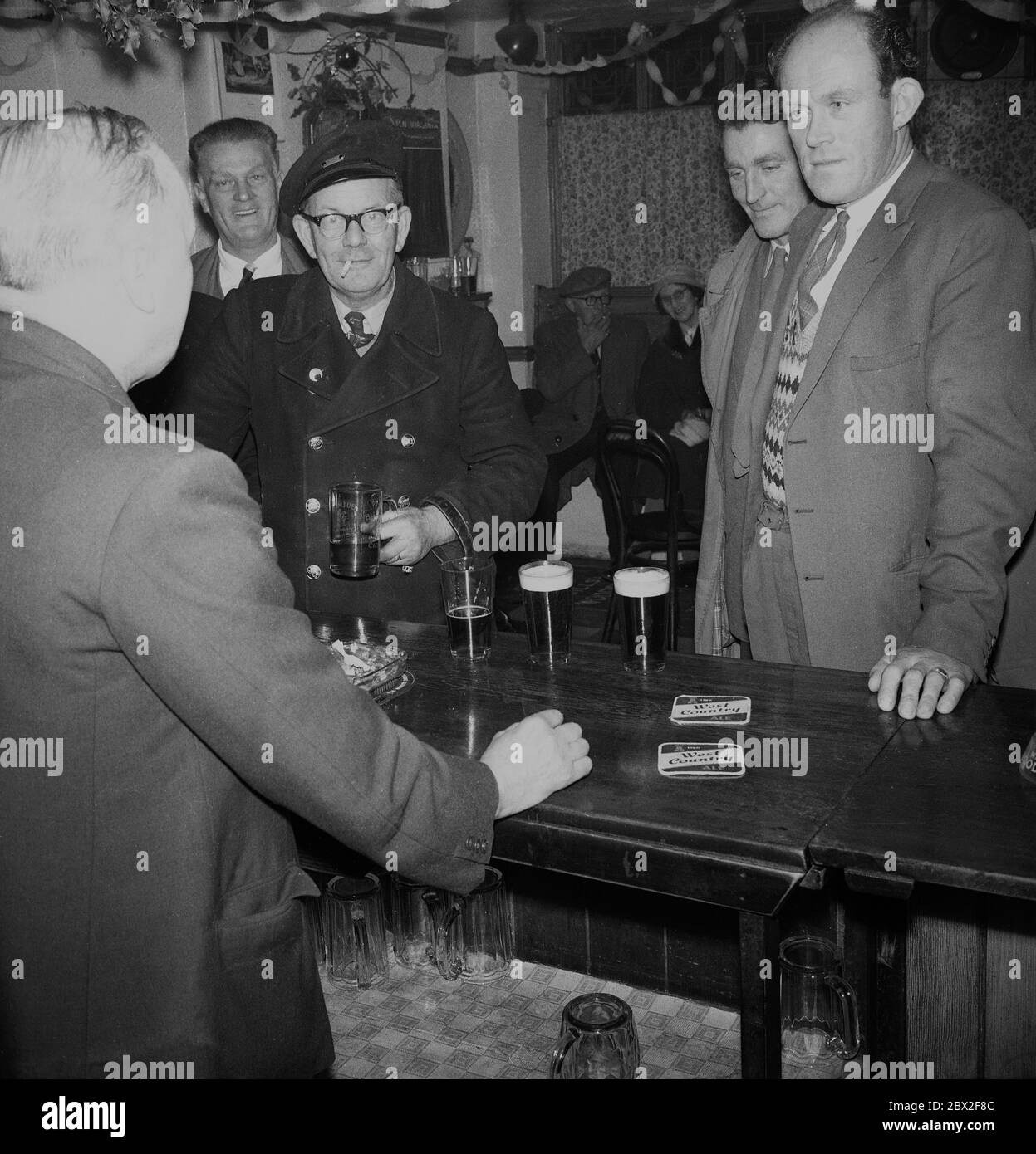 Anni '60, storici, uomini che bevono pinte di birra al bar di un pub che parla con il padrone di casa, con un Signore che tiene un tankard e fumare una sigaretta, Inghilterra, Regno Unito. Foto Stock