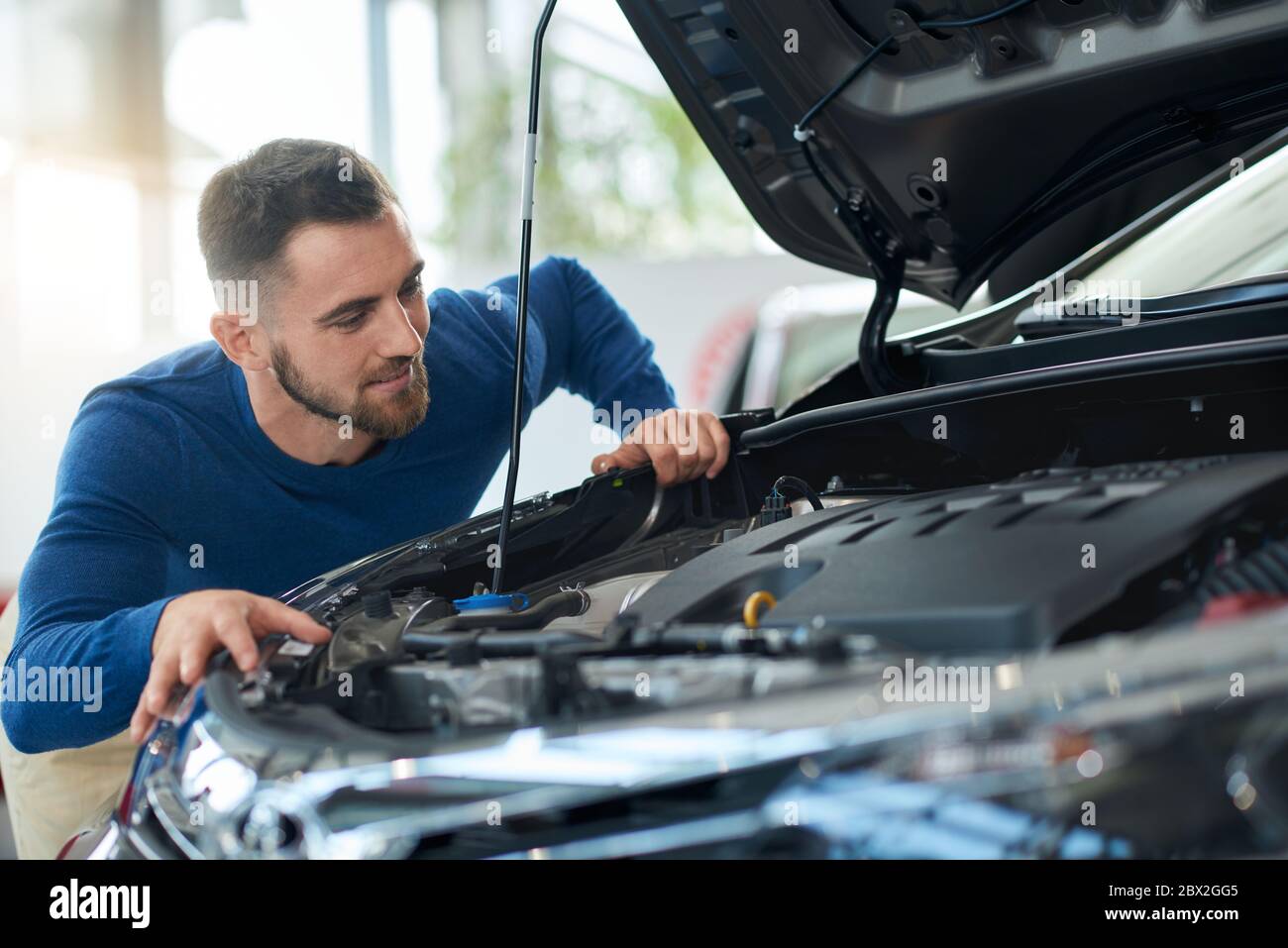 Felici sorridenti bei uomini in camicia guardando il cofano aperto dell'automobile prima di riuscito acquisto del veicolo. Primo piano di un giovane cliente maschile che sceglie l'auto per l'acquisto, il controllo del motore e i dettagli. Foto Stock