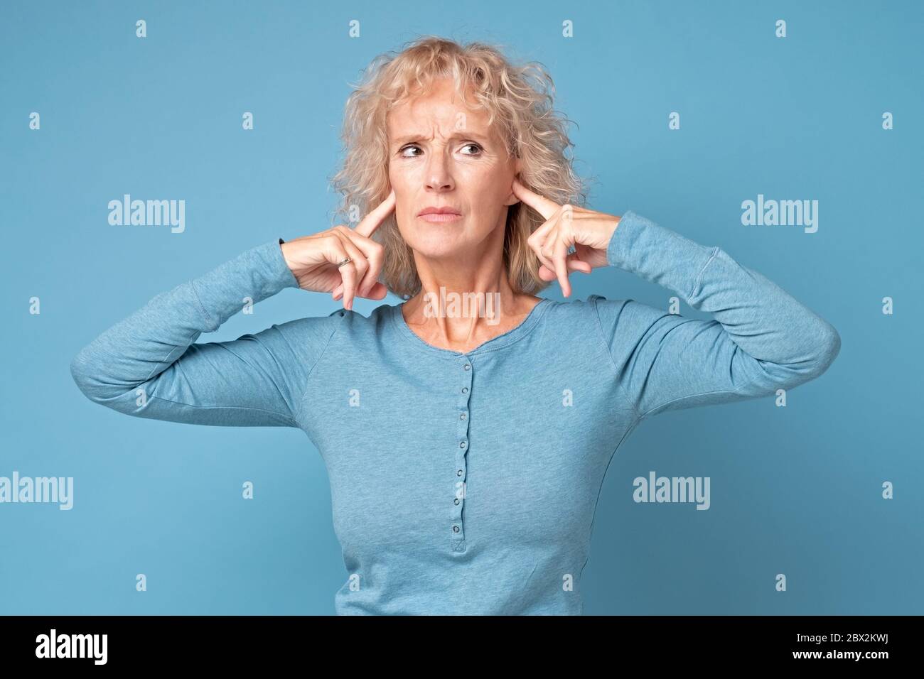 donna che indossa abiti blu che le ostruono le orecchie e vuole fermare il rumore forte. Foto Stock