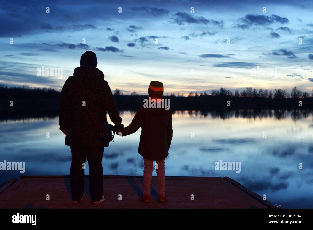Madre e bambino in piedi su un molo e guardando il tramonto su un lago Foto Stock