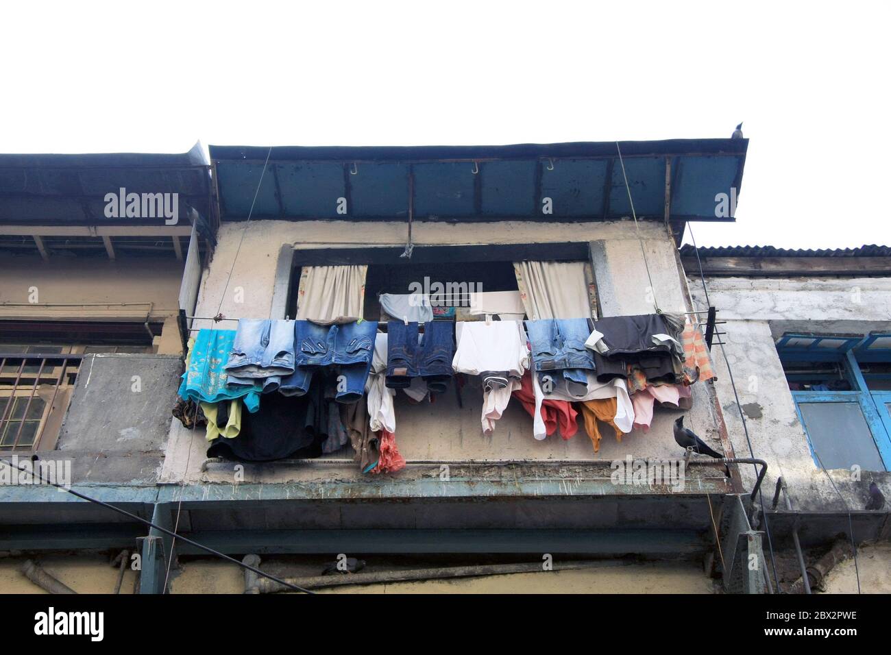Linea di lavaggio piena di vestiti appesi fuori una finestra di baraccopoli a Mumbai, India Foto Stock