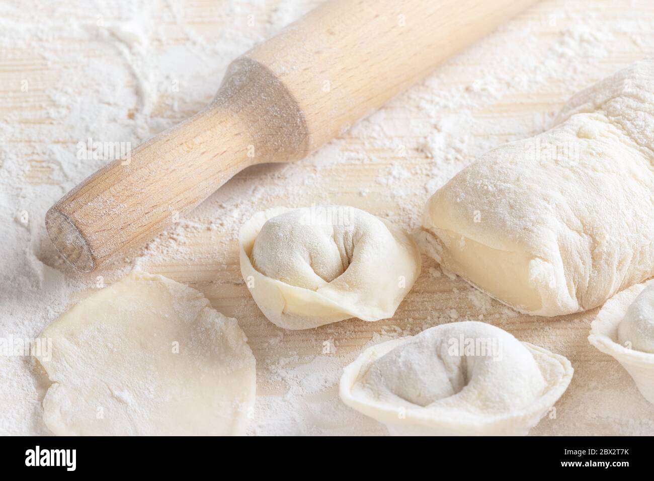 Ravioli italiani tradizionali crudi fatti in casa con carne e un mattarello su superficie di legno. Stappatura di gnocchi con carne macinata e impasto su ta Foto Stock