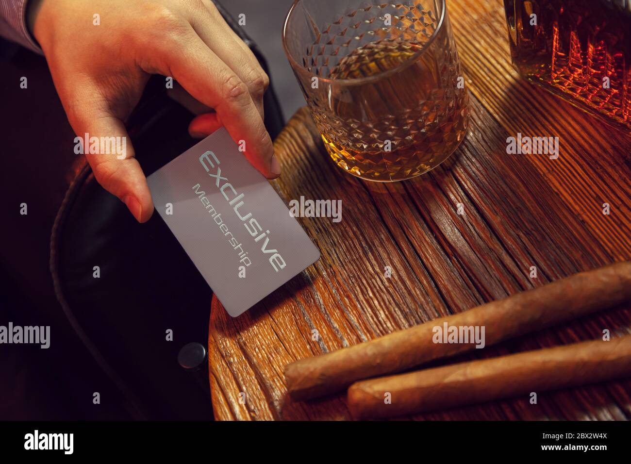 La mano dell'uomo mette la carta esclusiva di insieme dei membri sul tavolo. La mano del Signore mette la carta esclusiva di insieme dei membri sul tavolo di legno con il whisky in caraffa e. Foto Stock