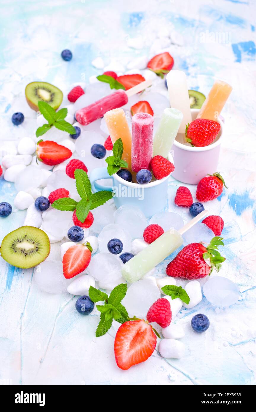 Papicle di frutta intera sane con fragole di Berries Kiwi su sfondo chiaro con un decor di ghiaccio, menta. Gustoso gelato alla frutta nella tazza. Spazio di copia. Foto Stock