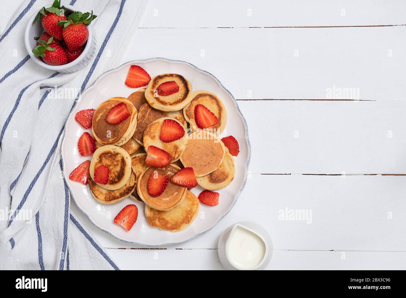 Vista dall'alto di mini frittelle con fragole su tavolo di legno bianco. Concetto di cibo sano con spazio per il testo Foto Stock