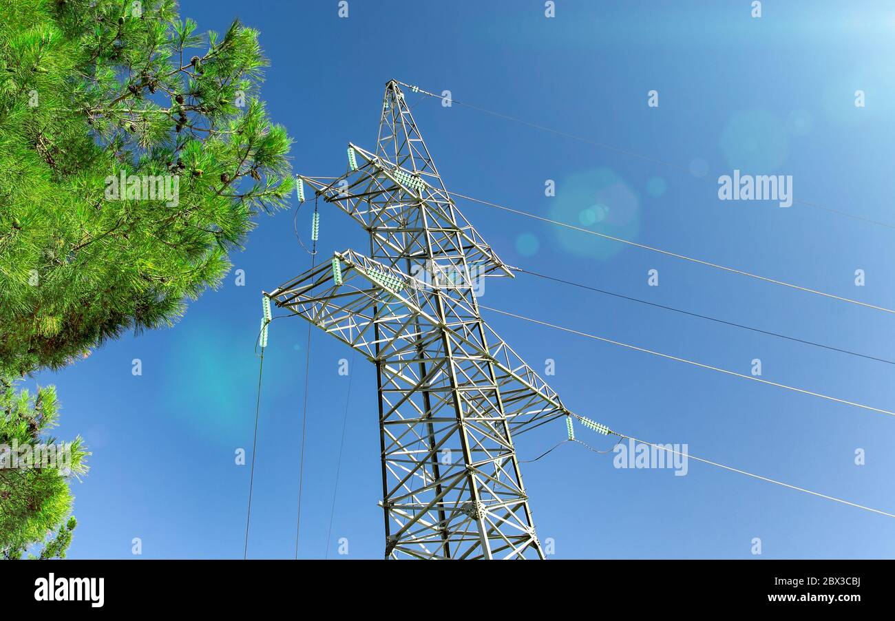 Pilone di trasmissione ad alta tensione contro un cielo blu, sole e rami verdi. Primo piano Foto Stock