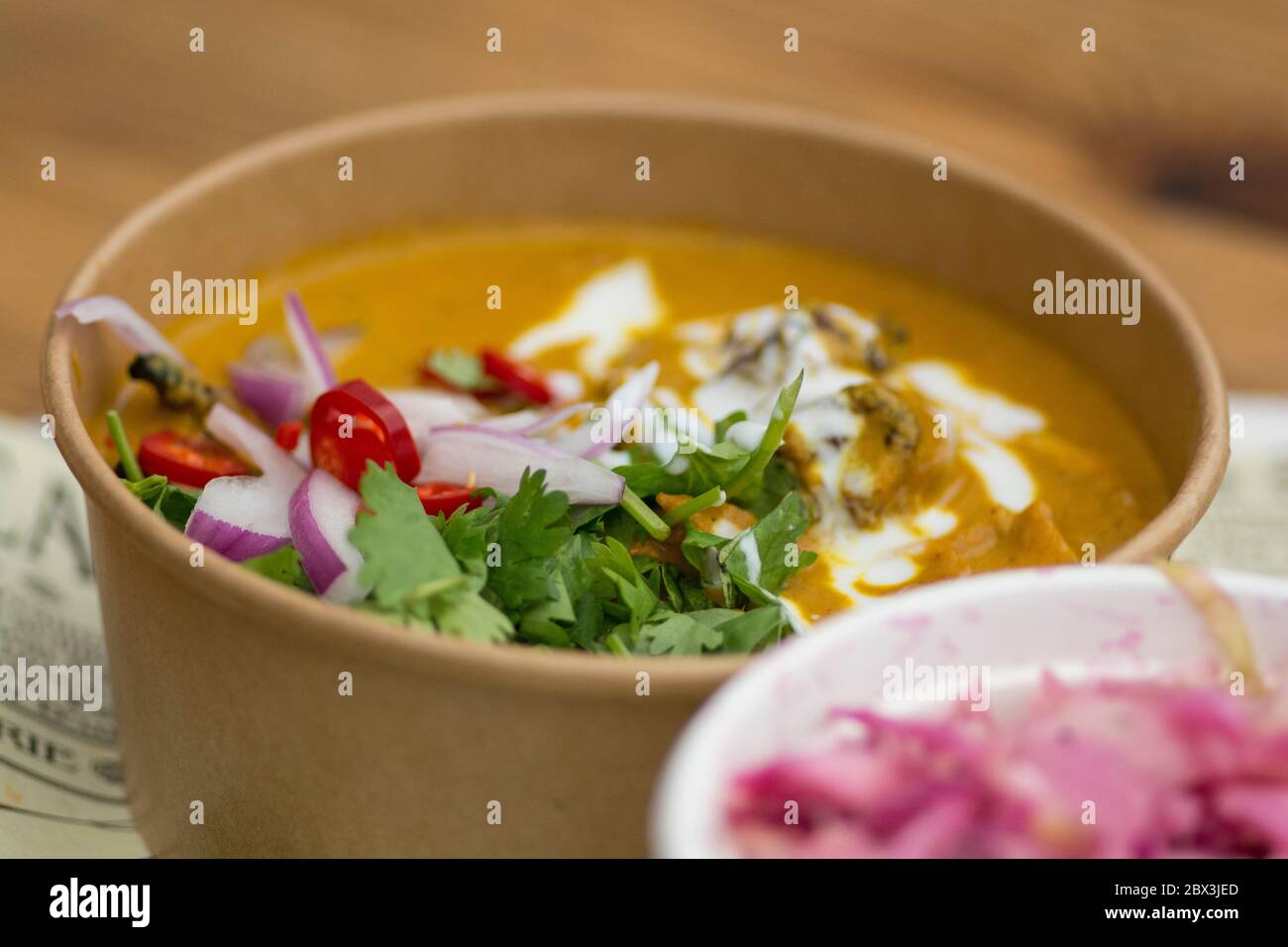 Vista dall'alto di un piatto di curry giallo indiano, con pezzi di carne di pollo, peperoni rossi piccanti, yogurt, cipolle rosse e foglie di coriandolo verde, serviti in un pa Foto Stock