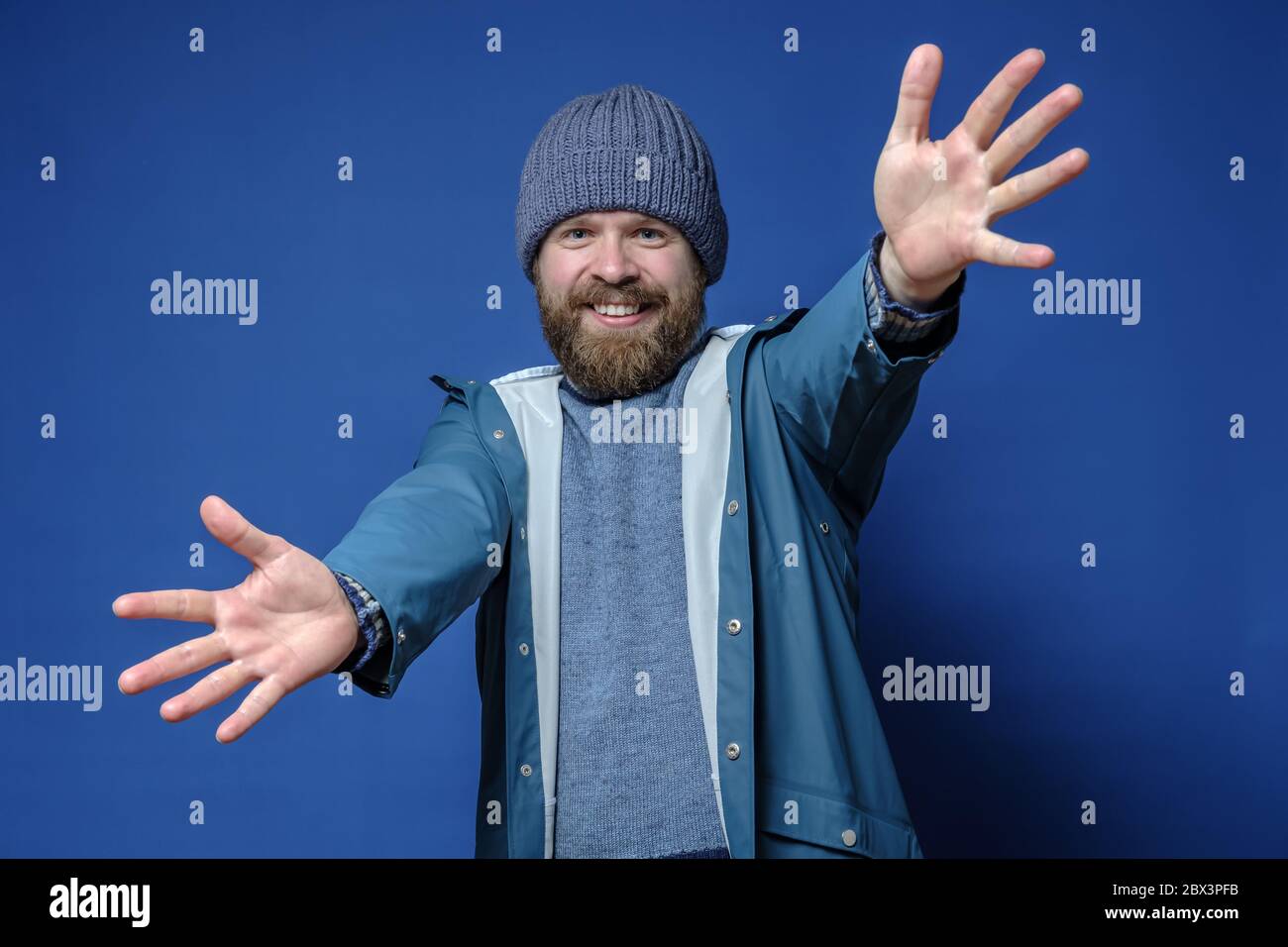 Felice, sorridente uomo bearded in un cappello e impermeabile è felice di incontrare e si alza con le braccia aperte per abbraccio. Foto Stock