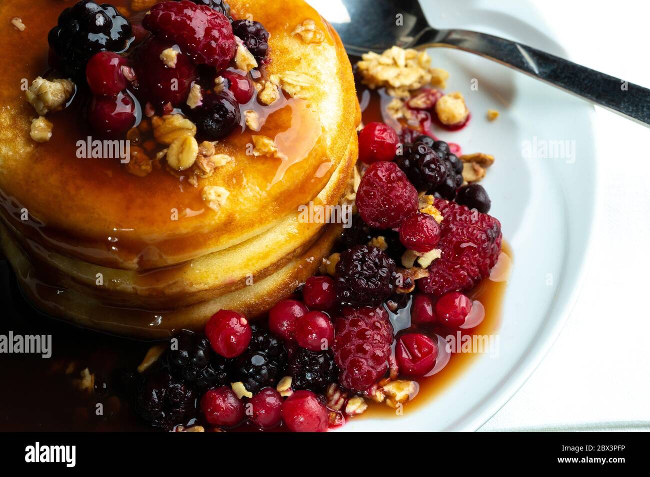 Primo piano di frittelle con frutti di bosco bacche su tavola di legno. Mirtilli, lamponi su frittelle con sciroppo d'acero. Concetto mattina proteine colazione Foto Stock