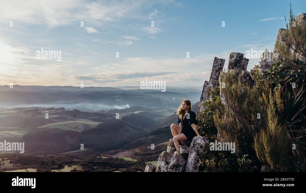 Foto aerea - bella donna asiatica sedersi e posare in cima alla Organ Pipes, Mt cargill Dunedin Nuova Zelanda. Foto Stock