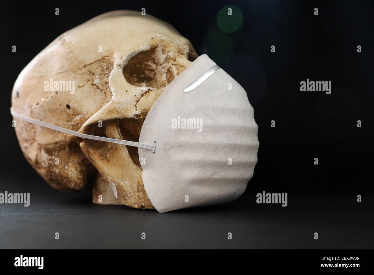 Cranio isolato su uno sfondo nero e scuro che indossa una semplice maschera di carta per la protezione contro la malattia dei fumi di odore o virus. Covid-19 corona Foto Stock