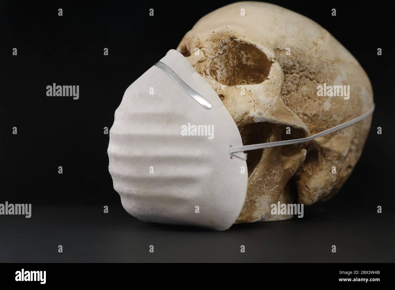 Cranio isolato su uno sfondo nero e scuro che indossa una semplice maschera di carta per la protezione contro la malattia dei fumi di odore o virus. Covid-19 corona Foto Stock