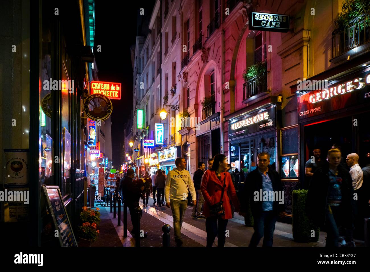 I turisti passano accanto a negozi e caffetterie mentre camminano per le colorate strade illuminate al neon di notte nel quartiere Latino di Parigi, Francia Foto Stock