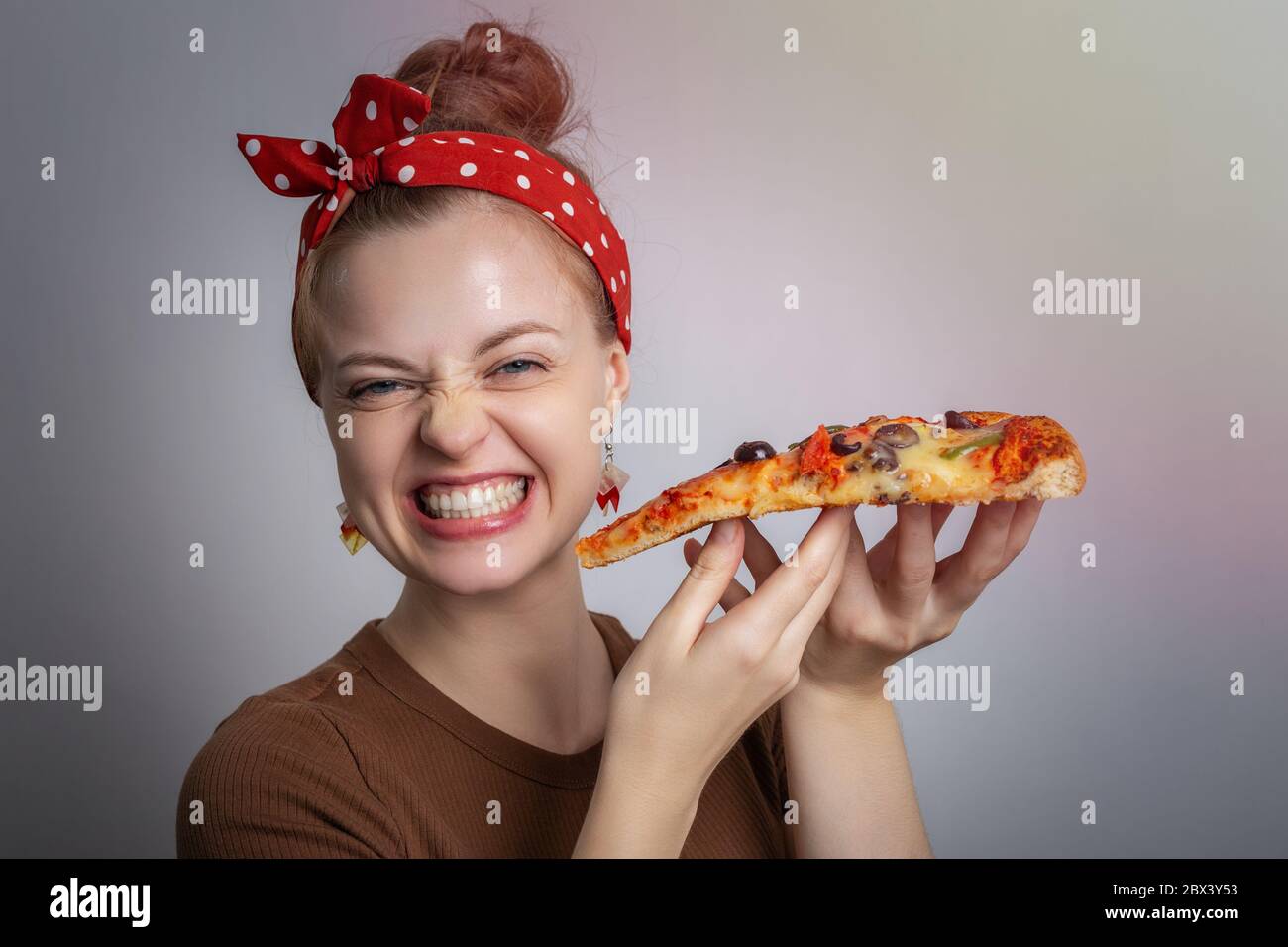 Sorridente giovane donna caucasica ragazza che tiene un grande pezzo di pizza. Concetto di consegna degli alimenti Foto Stock