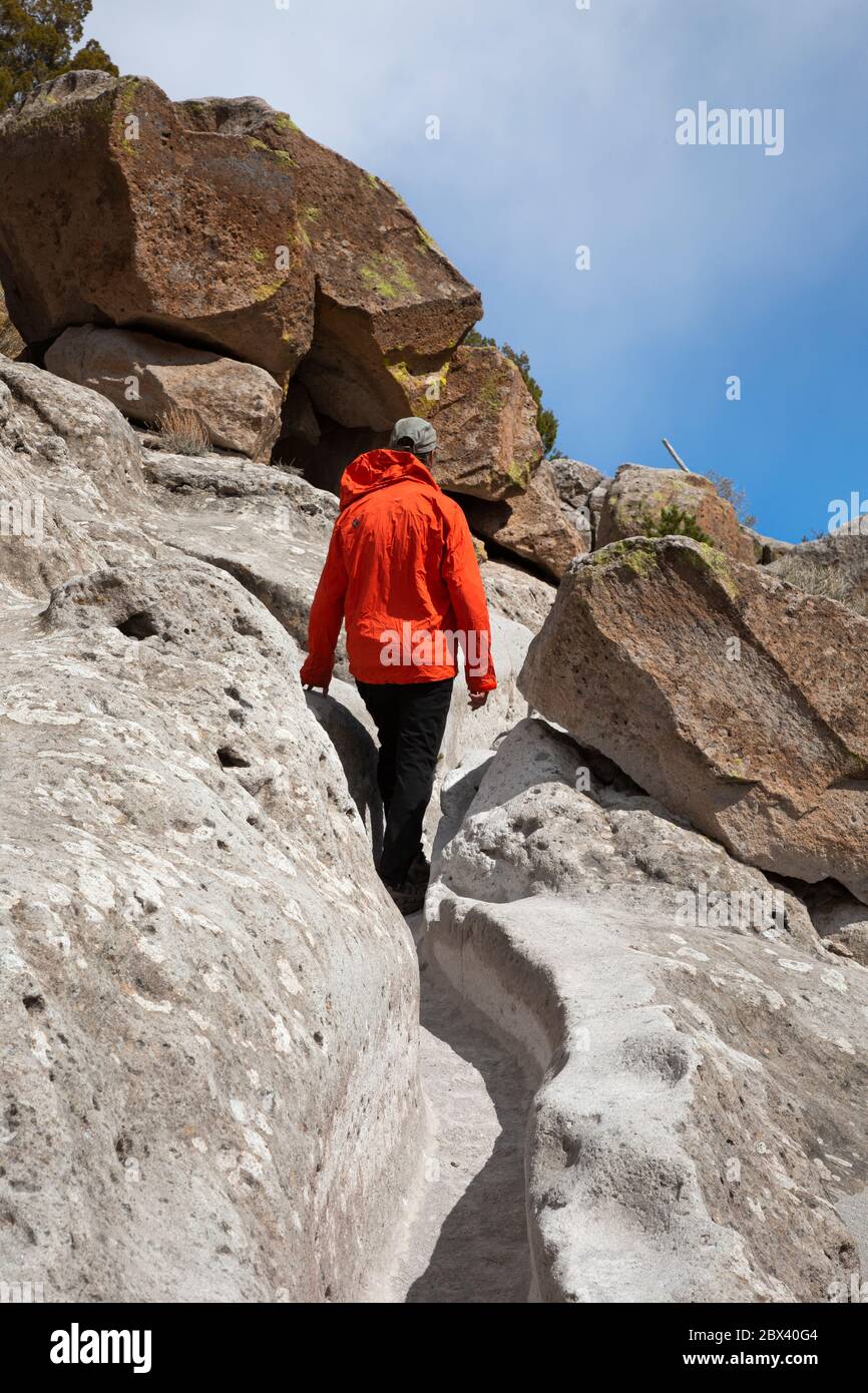 NM00501-00...NUOVO MESSICO - Hiker che cammina lungo lo stretto sentiero portato nella pietra morbida dai Puebloans ancestrali all'unità Tsankawi di Bandelier NM. Foto Stock