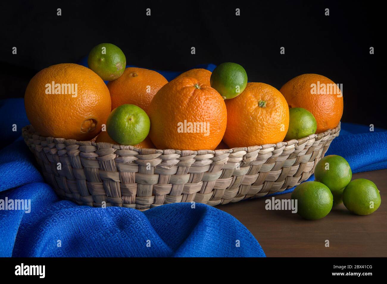 Ancora vita, luce bassa chiave, arance e limoni in un cestino messicano su un panno blu da tavolo Foto Stock