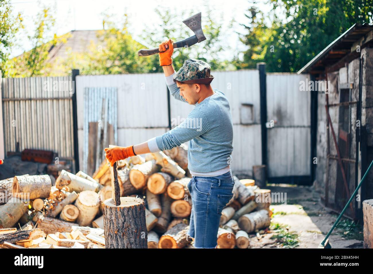 Uomo in jeans e camicia a scacchi in piedi vicino al moncone con ascia in mani Foto Stock