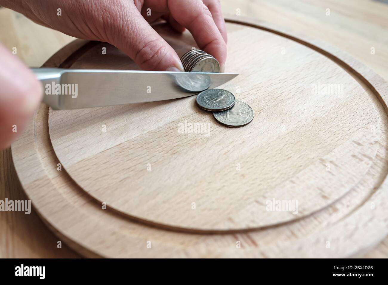 Le mani tagliano le monete del dollaro con un coltello, separandole come pezzi di cibo su un tagliere. Concetto di tasse, frode o profitto. Foto Stock