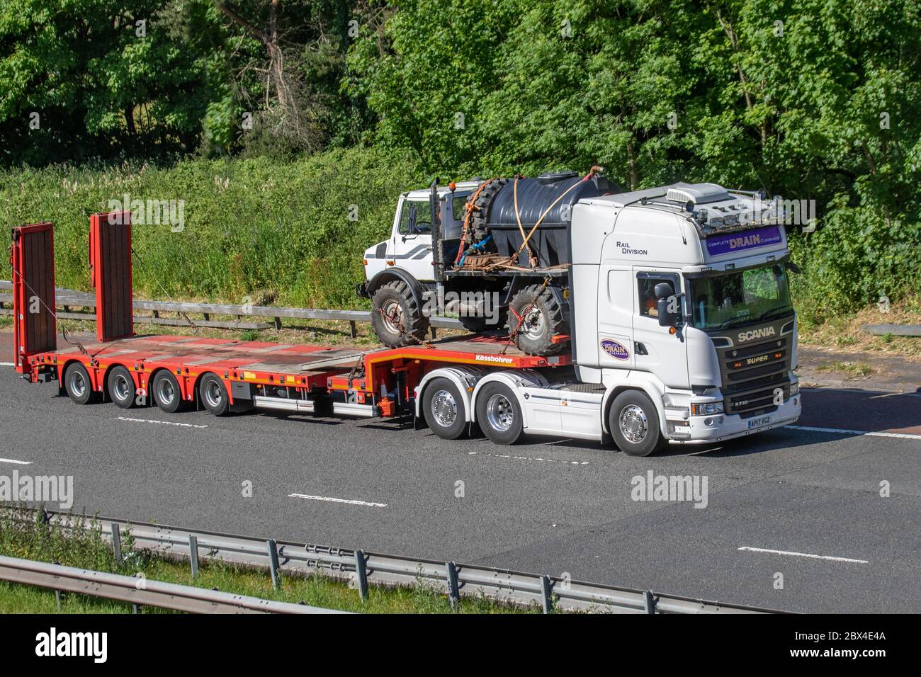 Servizi di scarico completi della divisione ferroviaria; autocarri per la consegna di merci, autocarri, trasporti, autocarri, cargo, veicoli Scania Super R730, industria europea del trasporto commerciale rimorchio HGV rimorchio Kassbohrer, che trasporta Unimog sulla M61 a Manchester, Regno Unito Foto Stock