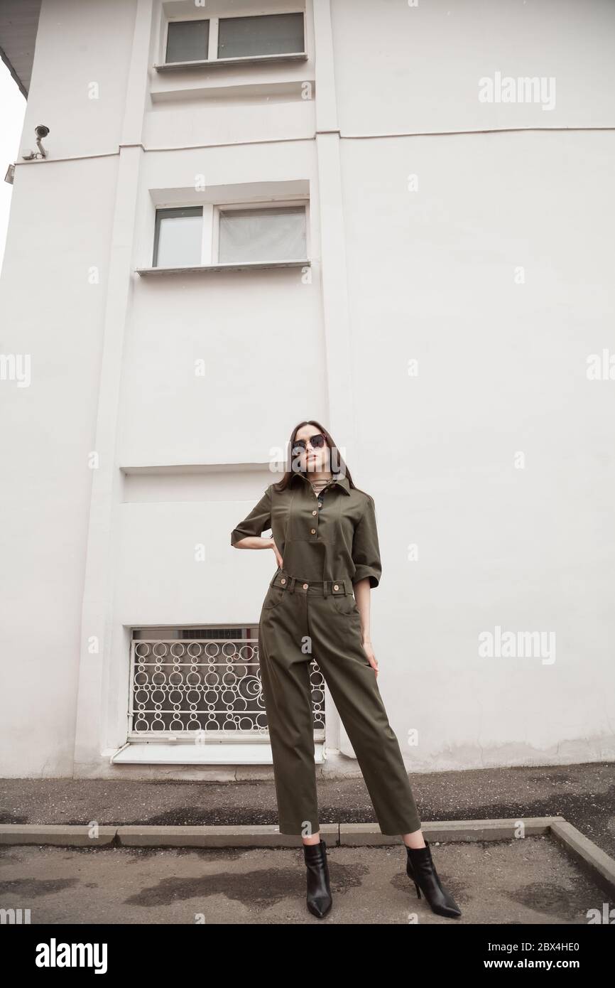 Ritratto di moda autunno esterno di giovane donna elegante con tuta pantaloni verde, in posa in strada della città europea. Spazio di copia parete bianca minimalista Foto Stock