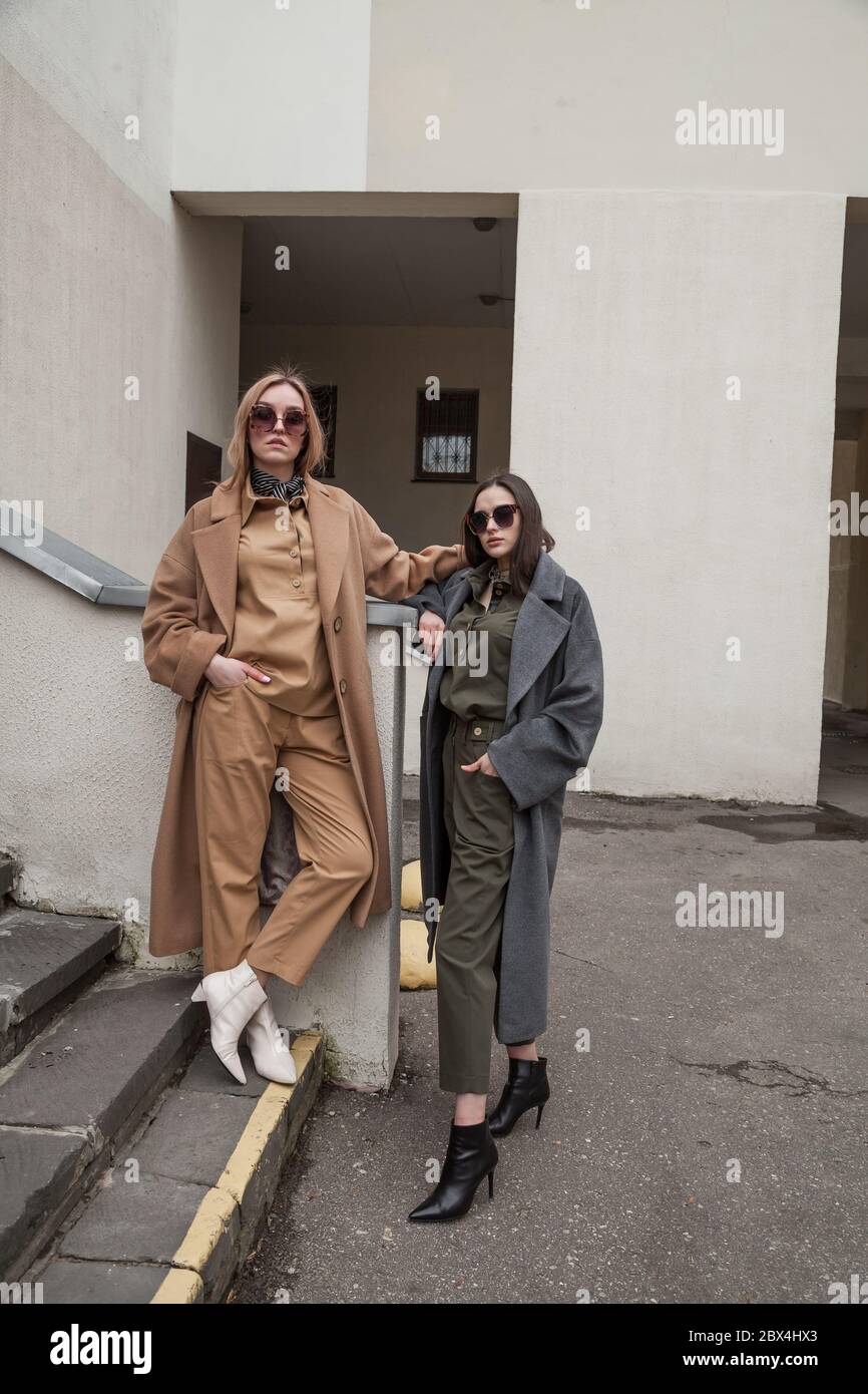 Ritratto di moda all'aperto di due giovani belle donne che indossano abiti alla moda, ridendo e guardando via, in posa in strada della città europea Foto Stock