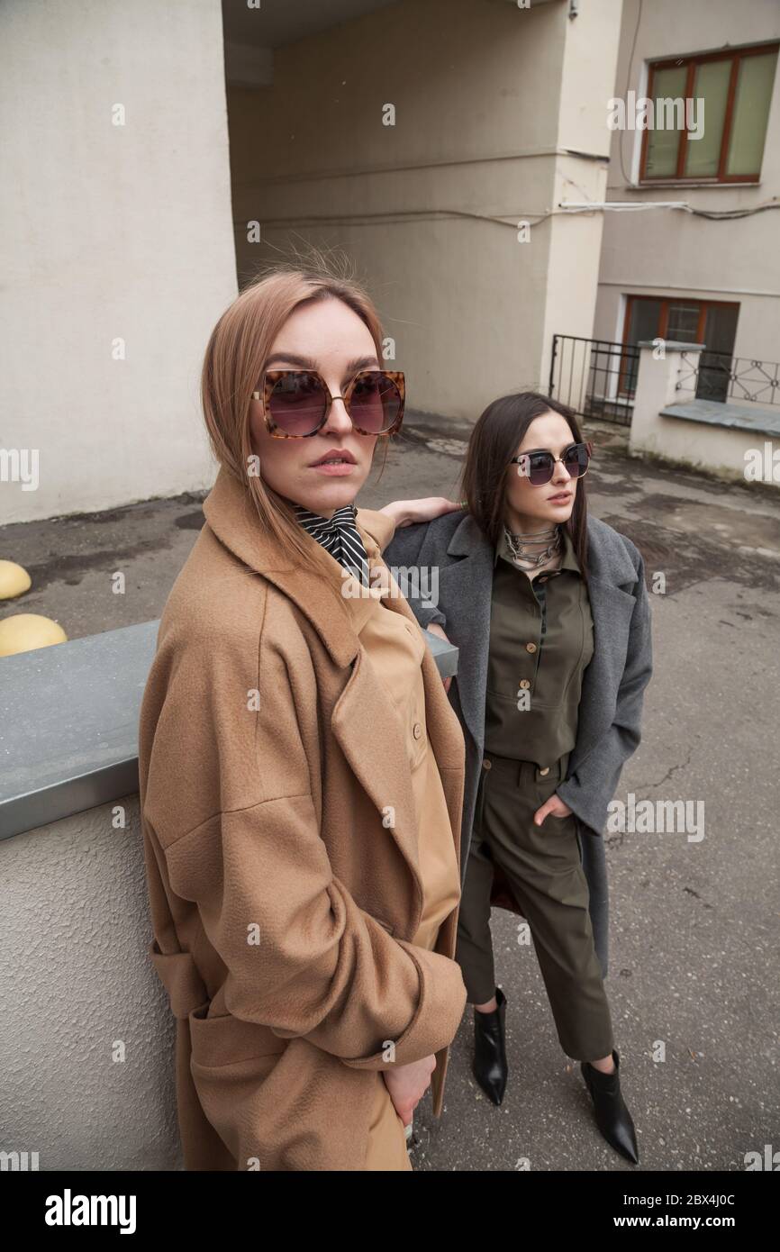 Foto di due belle donne alla moda in abiti caldi alla moda. Attraenti modelli femminili che si posano alla telecamera sullo sfondo della città Foto Stock