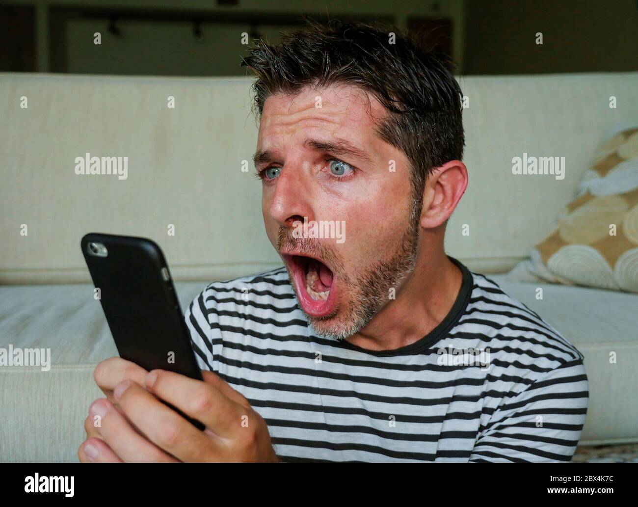 giovane uomo perplesso e scioccato utilizzando il telefono cellulare cercando internet social media o controllare le notizie in sorpresa e folle discredenza faccia espressione tassa Foto Stock