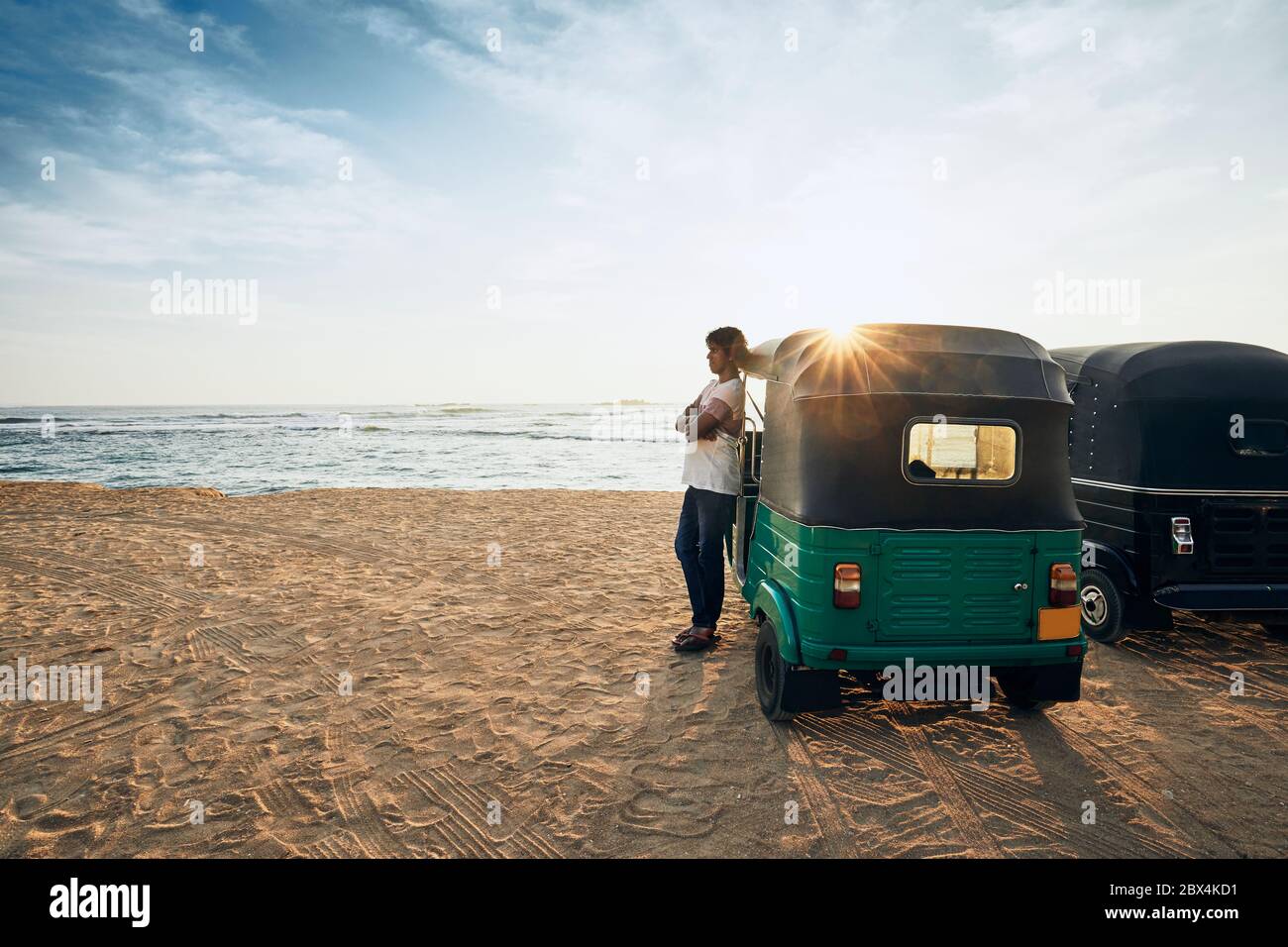 Autista in tuk tuk in attesa di passeggeri contro la spiaggia di sabbia e il mare. Unawatuna, Sri Lanka. Foto Stock