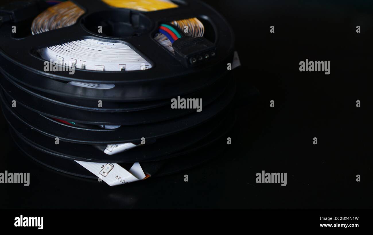 Bobine di striscia LED rgb su un tavolo nero. Striscia LED per un'illuminazione creativa raccolta in una bobina nera, strumenti per l'illuminazione e gli effetti luminosi. Foto Stock