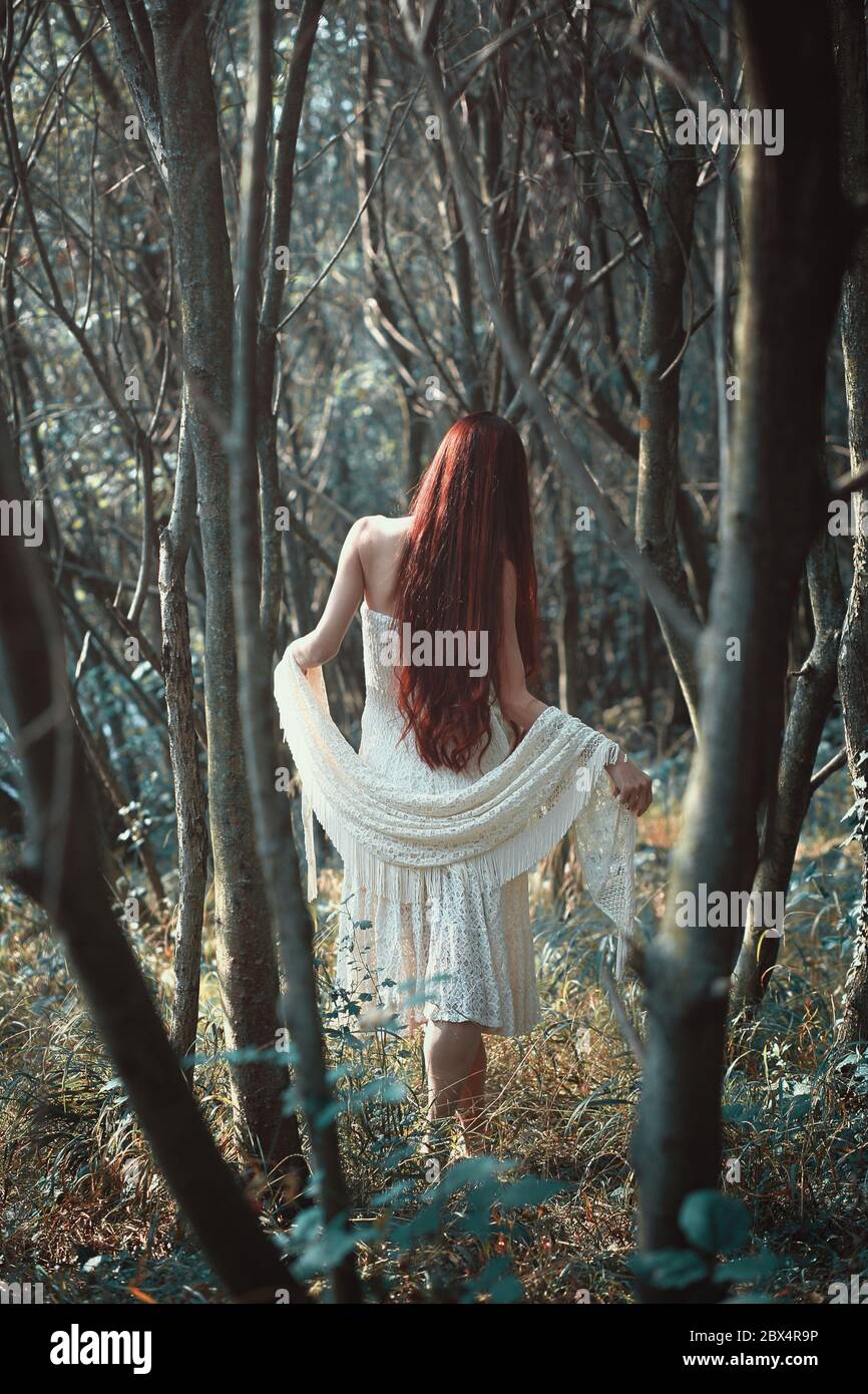 Donna con lunghi capelli rossi cammina nella foresta strana . Etereo e romantico Foto Stock
