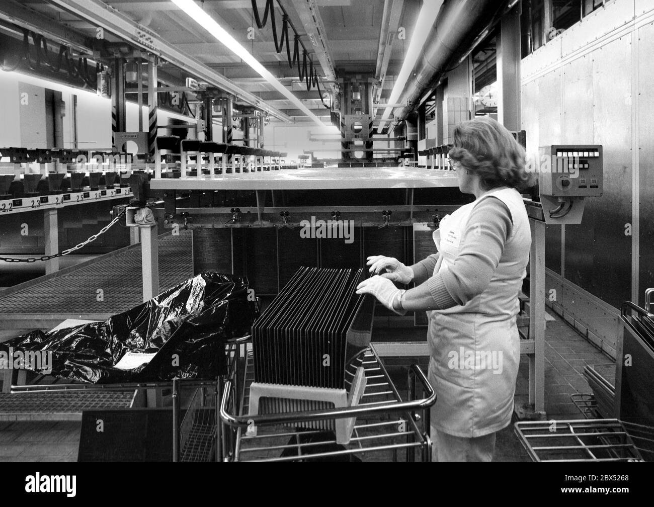 Berlin / Kreuzberg / 17.10.1980 DeTeWe: L'azienda produce armadi per uffici postali. Le donne producono parti in prefabbricazione. Nella prossima generazione di tecnologie, questo lavoro sarà svolto da macchine automatiche. Donna al negozio di elettroplastica. Nelle file di bagni chimici, le schede a circuito stampato sono incise. La donna posiziona le piastre sui nastri trasportatori. // lavoro femminile / Storia industriale / [traduzione automatizzata] Foto Stock