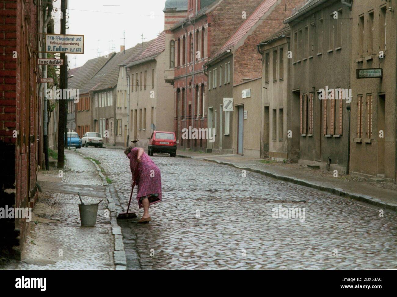 Brandeburgo / DDR / inizio 1990 Jueterbog, città vecchia, strada centrale. Una donna trasla la strada di fronte alla sua casa // Teltow-Flaeming / Stati federali / GDR-Land [traduzione automatizzata] Foto Stock