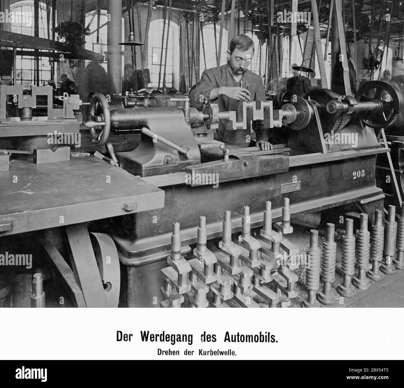 Un lavoratore esperto in una fabbrica di automobili al tornio mentre fa girare un albero a gomiti, che misura con il calibro per la precisione. Foto Stock