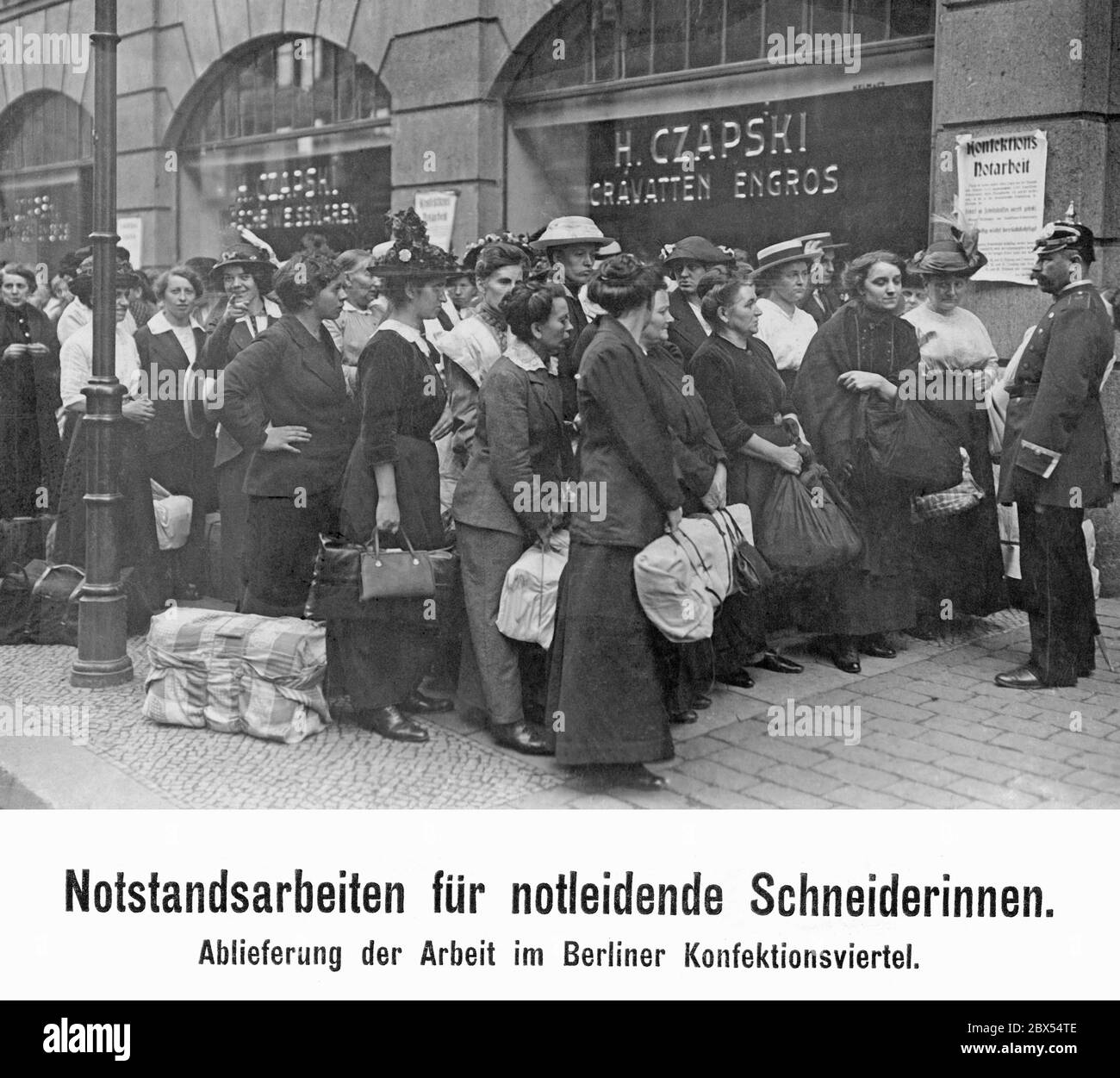 I marinai bisognosi consegnano i loro lavori pubblici di soccorso nel quartiere dell'abbigliamento di Berlino. Mentre milioni di uomini sono stati redatti allo scoppio della guerra, molti dei principali vincitori delle famiglie sono scomparsi. I fondi statali non hanno compensato a sufficienza tale situazione. Lo Stato ha quindi creato lavori di soccorso e obblighi di servizio per aiutare. Sullo sfondo, il negozio H.Czapski. Sul muro è un poster con un annuncio sul lavoro pubblico di soccorso nel settore dell'abbigliamento. Foto Stock