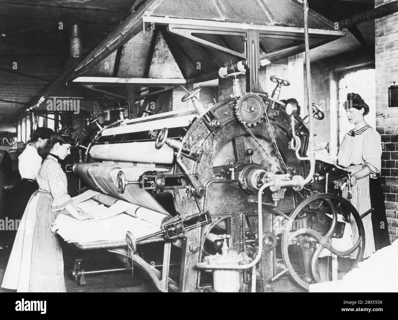 Una delle prime lavanderie di Berlino mostra ai dipendenti che rotolano la lavanderia appena lavata in quella che allora era una macchina da stiro a vapore molto moderna. Foto Stock