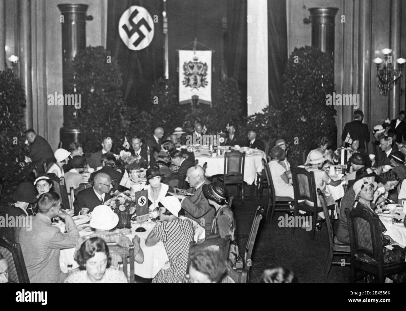 Tedeschi ed inglesi si siedono insieme ai tavoli rotondi e chiacchierano durante un tè. Sullo sfondo e sui tavoli sono le bandiere swastika. 170 studenti di scuola notturna inglese, rispettivamente studenti di istruzione per adulti che si trovano in Germania per scopi di studio, sono invitati a prendere un tè nel municipio di Berlino. Foto Stock