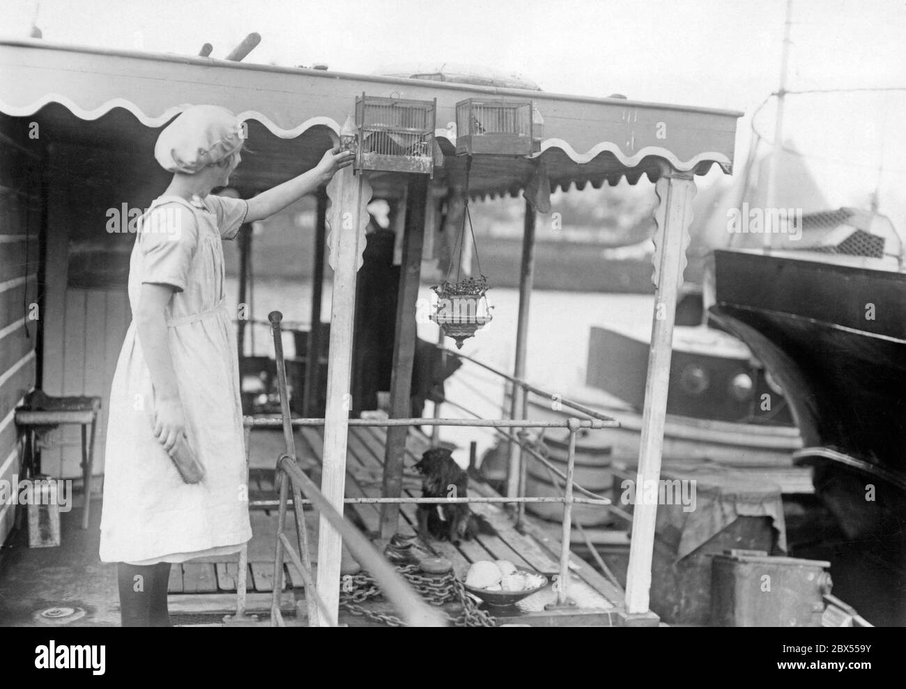 Una donna operaia in un grembiule bianco e cappuccio sta alimentando gli uccelli su una chiatta. Queste vecchie chiatte per il trasporto merci sono state utilizzate come abitazioni a causa della carenza di alloggi. Foto Stock