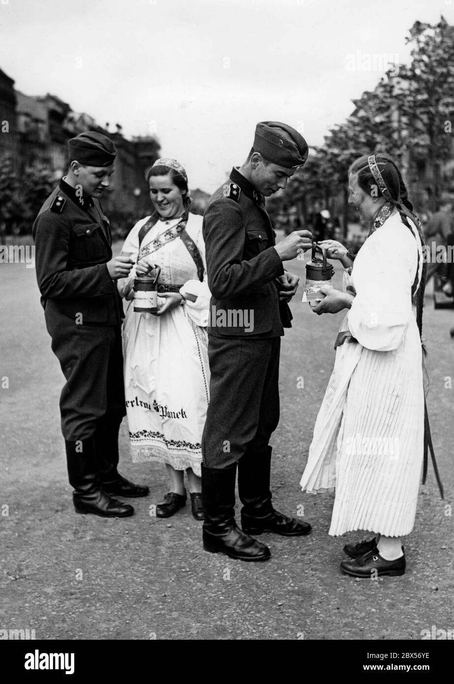 Gli uomini del Leibstandarte-SS Adolf Hitler acquistano uno stemma cittadino dai collezionisti VDA che indossano un costume popolare come donazione. Foto Stock