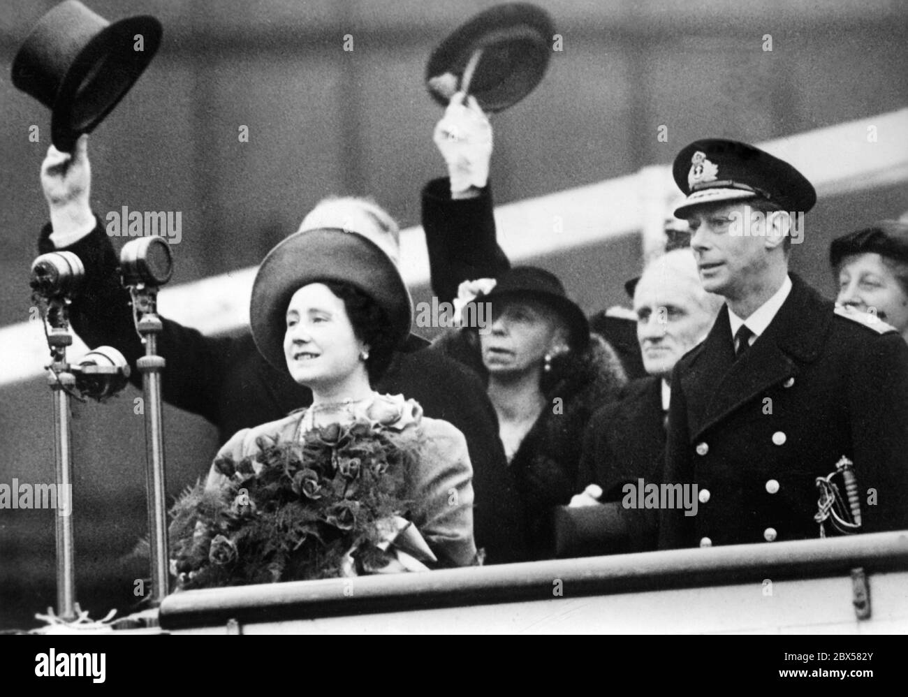 La regina Elisabetta e il re Giorgio VI si ergono sul palco. Dietro di loro gli uomini si capovolgono i loro cappelli. Foto non datata, ca. 1939 Foto Stock