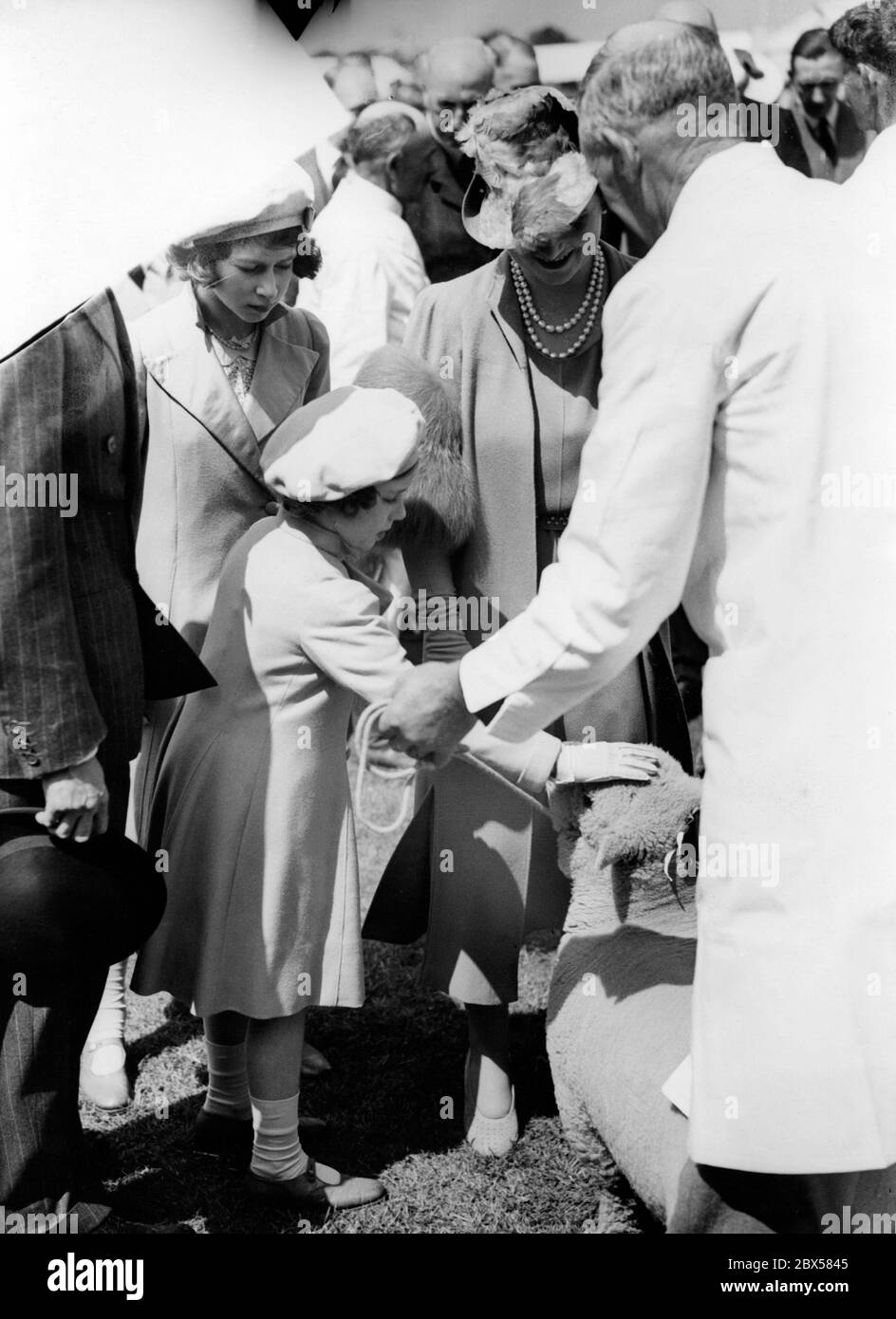 Elizabeth II con la sorella Margaret Rose, la regina Elisabetta (destra) e il re George VI (sinistra, testa coperta) al Centenary Show della Royal Agriculture Society a Windsor Great Park, Berkshire. Margaret sta stropicciando una pecora Southdown. Foto Stock