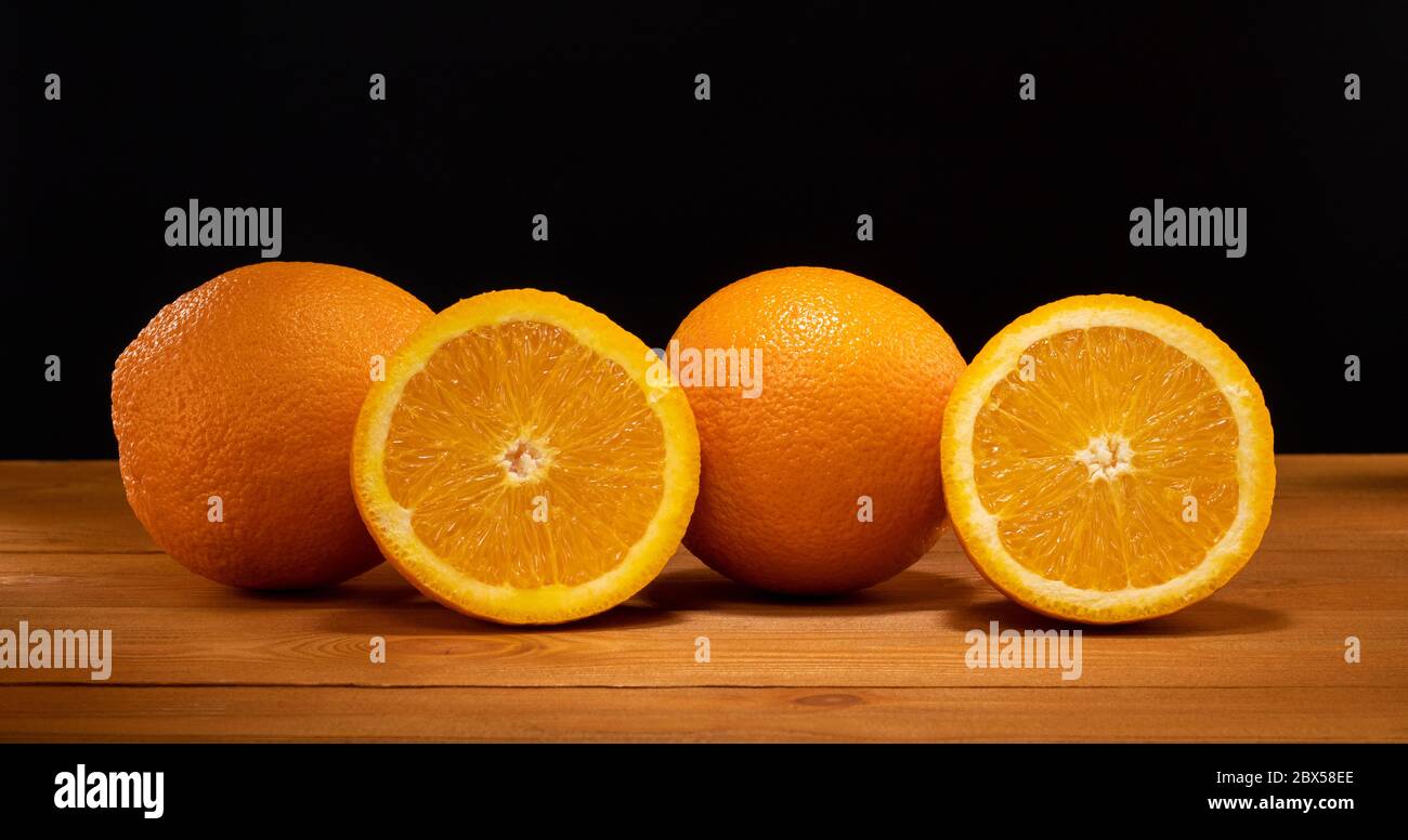 Metà fresca e succosa e fetta di frutta arancione su un tavolo di legno e sfondo nero. Foto Stock