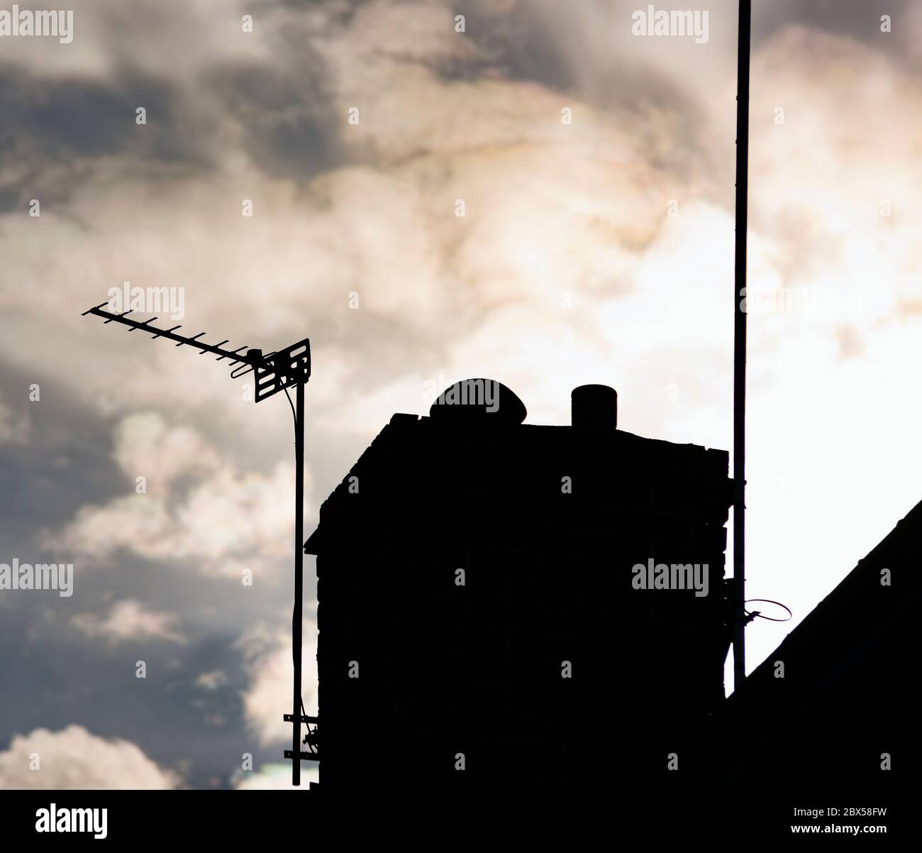 Silhouette di un'antenna televisiva e camino contro un cielo nuvoloso Foto Stock