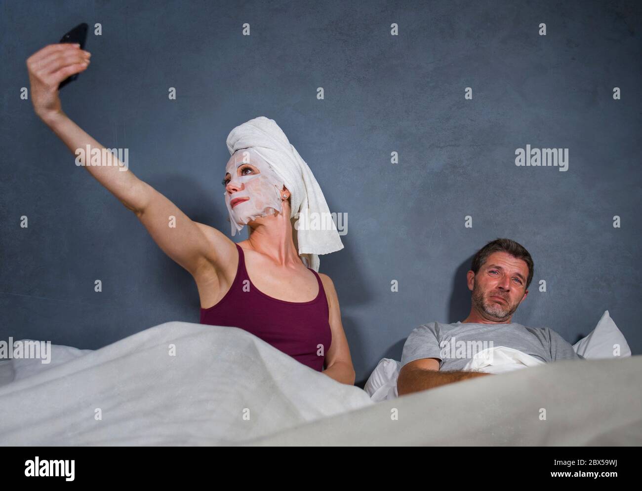 ritratto divertente stile di vita di casalinga eccentrica con maschera  trucco e asciugamano prendendo selfie a letto e marito con espressione  disperata del volto in w Foto stock - Alamy