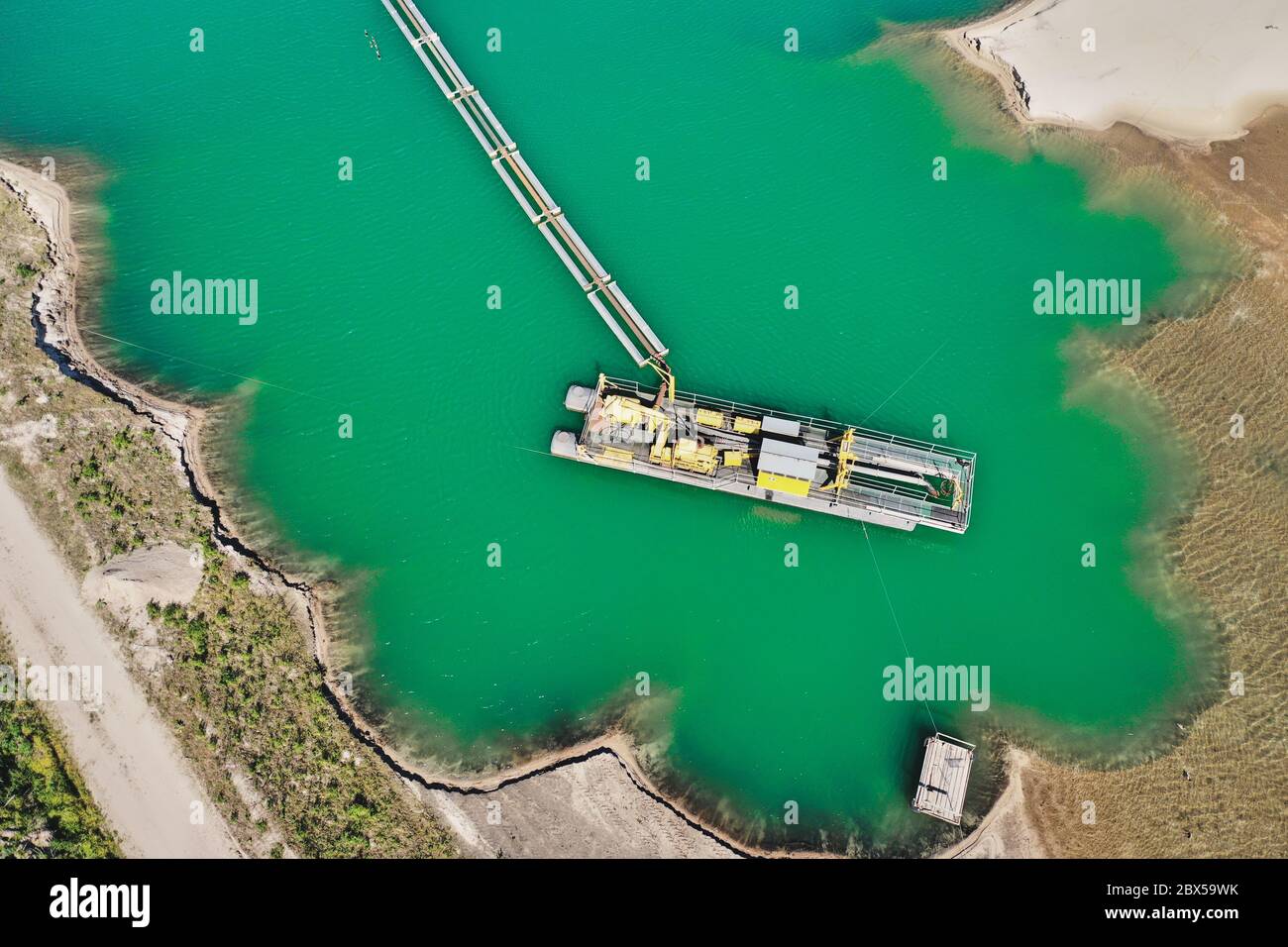 Fotografia aerea verticale di una draga aspirante in un'area mineraria umida per sabbia e ghiaia, con tubazioni collegate per rimuovere la sabbia Foto Stock
