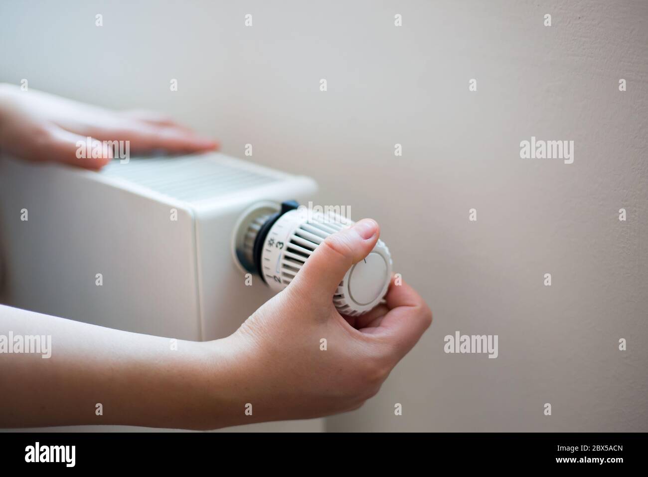 Donna che modifica la temperatura sul radiatore mediante il controller della temperatura, aumenta o diminuisce il prezzo del riscaldamento Foto Stock