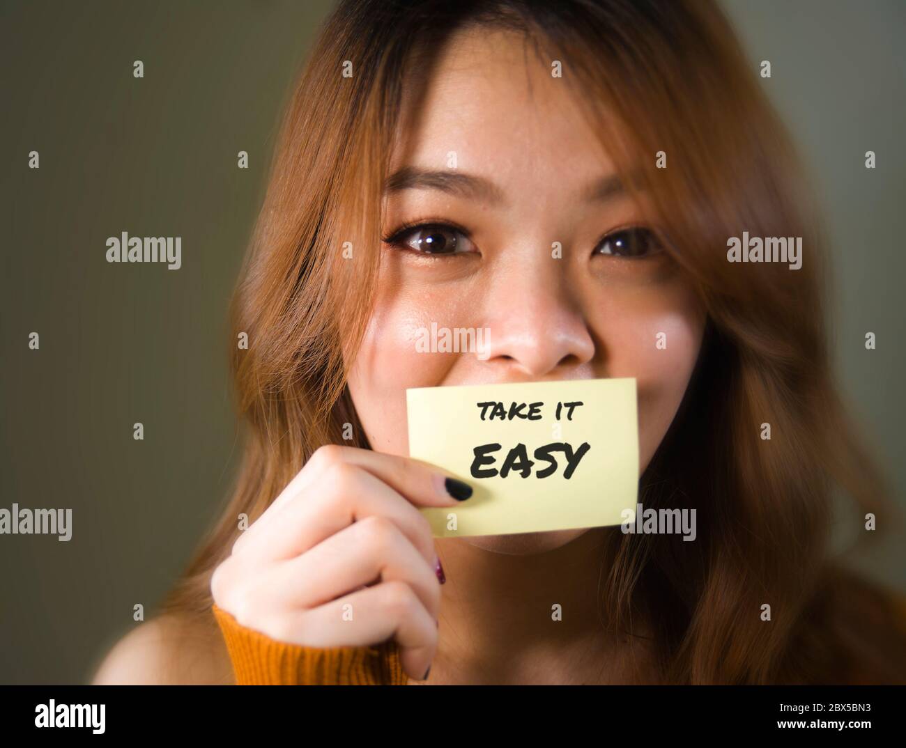 Primo piano ritratto faccia di giovane felice e bella ragazza coreana studentessa asiatica tenendo nota messaggio di testo con Take IT Easy handwritten sensazione eccitato Foto Stock