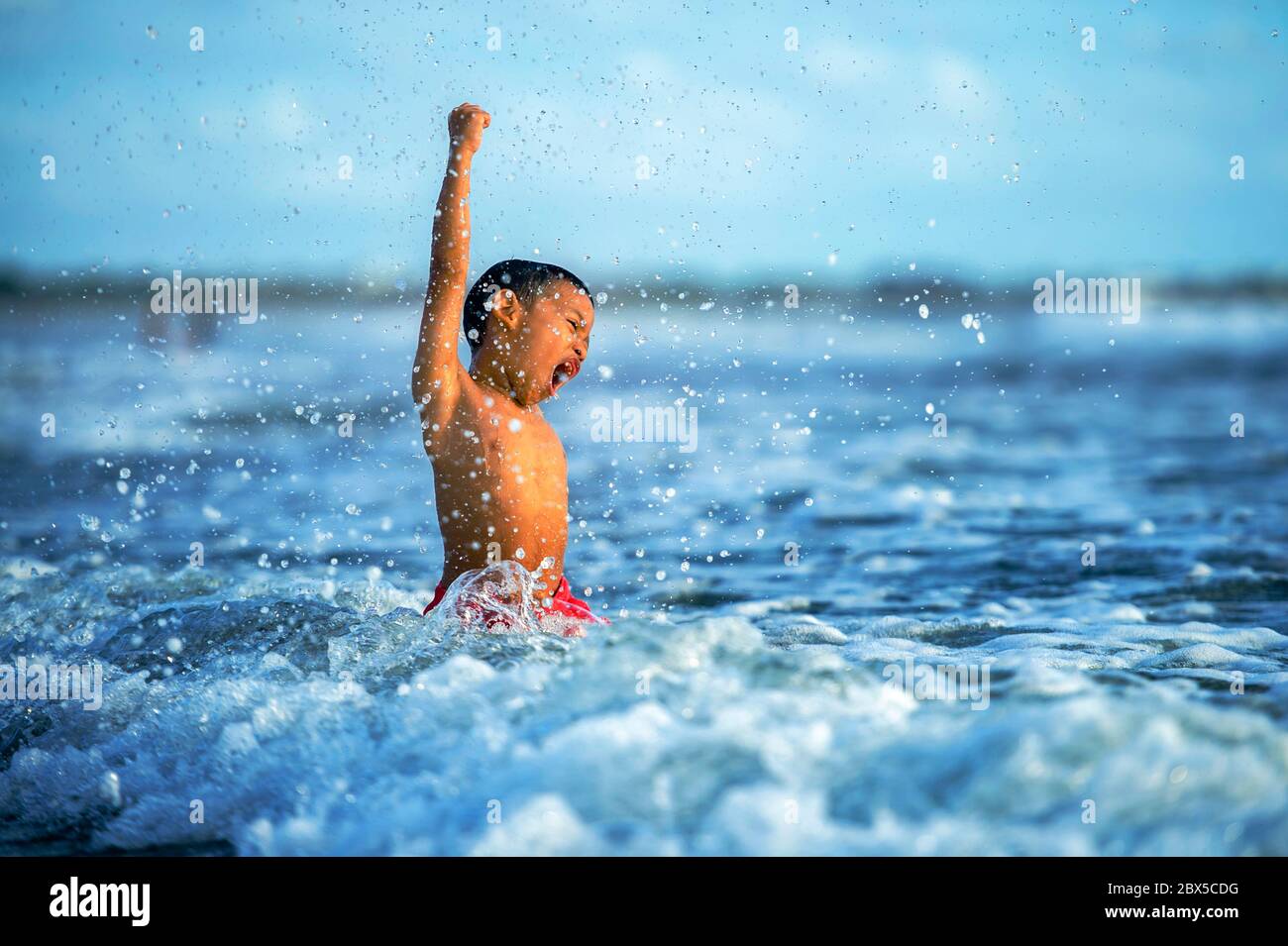 5 anni cute e felice bambino giocare pazzo libero divertirsi sulla spiaggia spruzzi d'acqua e mare onde godere di vacanze eccitate e allegre in Foto Stock